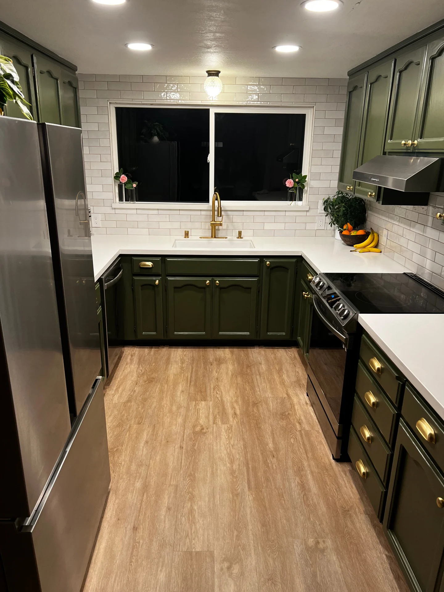 Galley kitchen with green cabinets and a white subway tile backsplash, with warm toned plank flooring