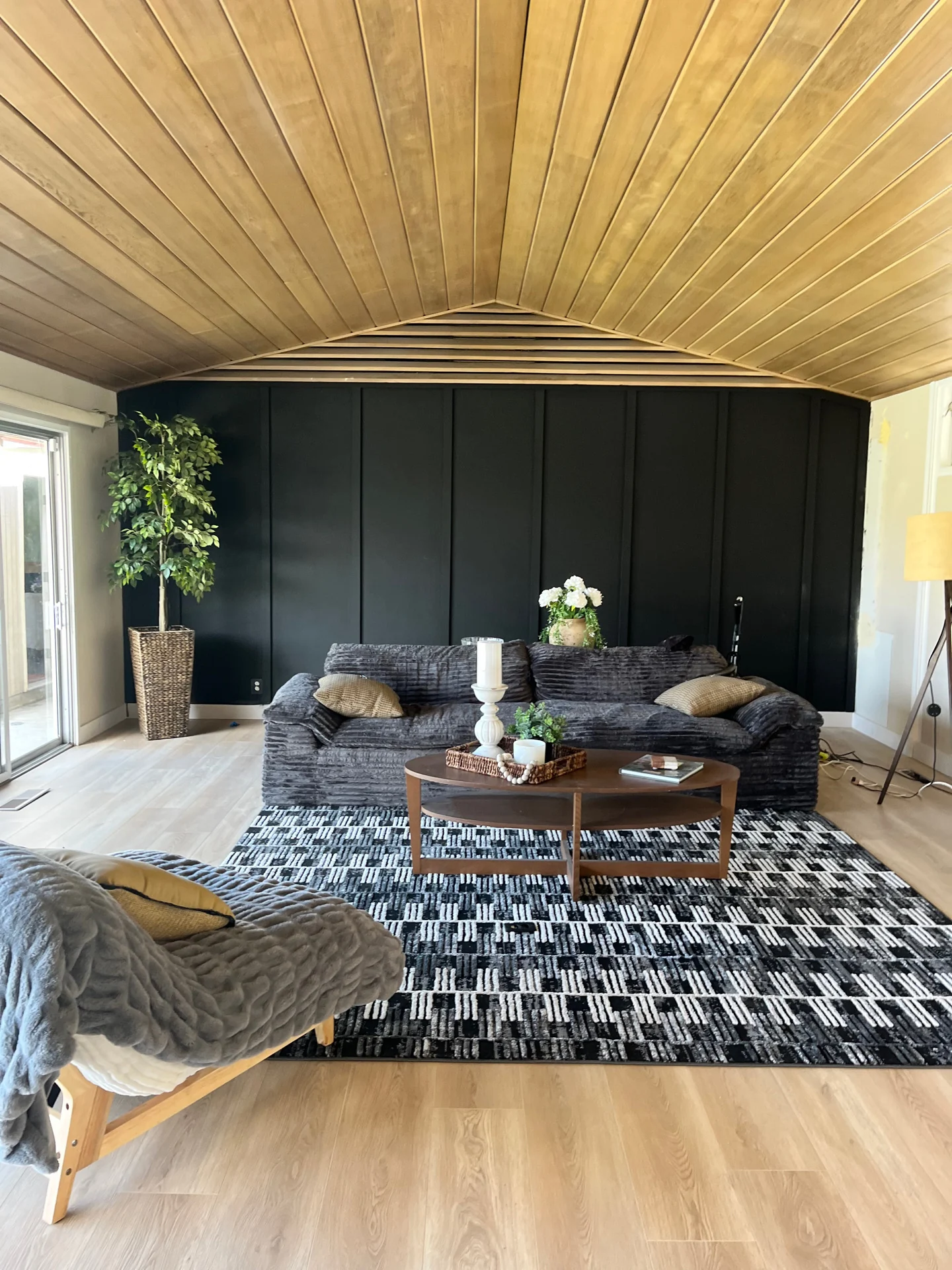 Living room with a plank ceiling and black accent wall over light plank flooring